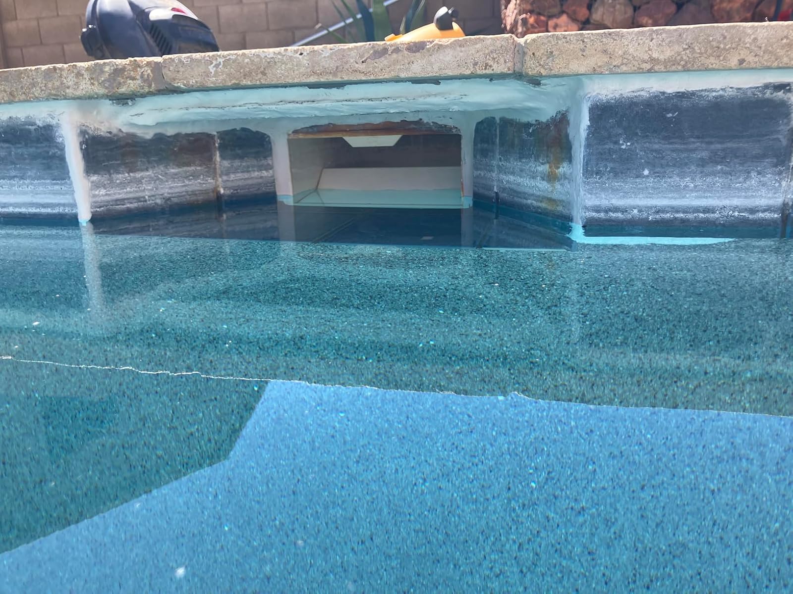 Pool skimmer mouth repaired with Epoxybond putty, water still at its normal level against a blue pebble finish